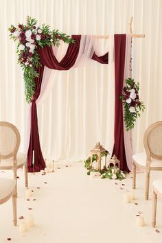 a wedding ceremony setup with white chairs and red drapes on the back drop cloth