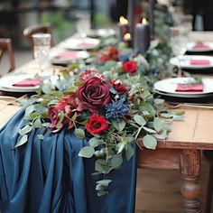 the table is set with red and blue flowers, greenery, and silverware