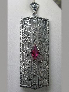 Ruby Pendant Necklace, Rectangle Art Deco style pendant with fine lace filigree and a diamond shaped red ruby gemstone in the center of the filigree, Silver Embrace Jewelry Vintage Necklace With Rectangular Pendant For Anniversary, Vintage Necklaces With Rectangular Pendant For Anniversary, Red Art Deco Hallmarked Jewelry, Art Deco Silver Jewelry With Large Pendant, Silver Art Deco Jewelry With Large Pendant, Silver Filigree Jewelry For Vintage Events, Art Deco Antique Silver Jewelry For Anniversary, Collectible Red Filigree Jewelry, Vintage Ruby Pendant Jewelry