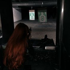 a woman with long red hair is shooting at an object in the dark, while another person stands near her