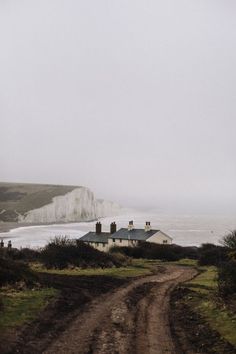 a dirt road leading to a white house on the side of a cliff by the ocean