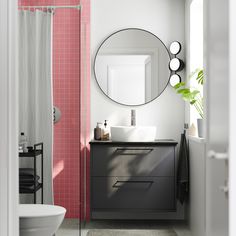 a bathroom with pink tiles and a round mirror above the sink, along with a white toilet