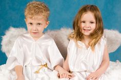 two young children dressed in white sitting next to each other with angel wings on them