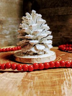 a pine cone sitting on top of a wooden table next to red beaded necklaces