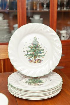 a stack of white plates with a christmas tree on the front and bottom, sitting on top of a wooden table