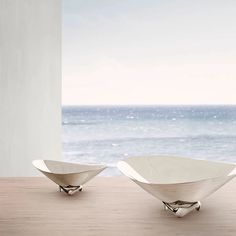 two white bowls sitting on top of a wooden table next to an ocean and sky background