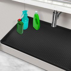 two green and blue bottles are sitting on a black mat in front of a sink