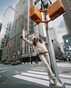 a woman hanging from a street light pole in the middle of a city with tall buildings