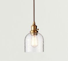 a small glass light hanging from a ceiling fixture with a brass finish and an exposed bulb