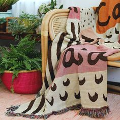 a chair with a blanket on top of it next to plants and potted plants