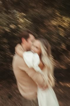 a man holding a woman in his arms while she is walking through the grass and trees