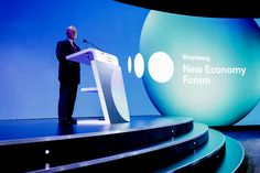 a man standing at a podium in front of a blue screen with the words new economy forum on it