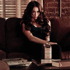 a woman sitting on a couch with a bottle of liquor in her hand next to books