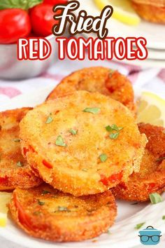 fried red tomatoes on a white plate with lemon wedges and cherry tomatoes in the background