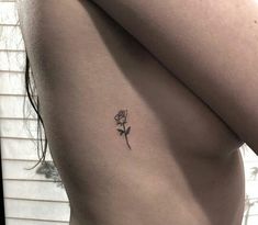 a woman's back with a single rose tattoo on her left side ribcage