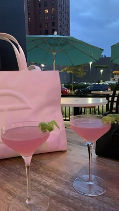 two martini glasses sitting on top of a table next to a pink bag and umbrella