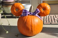 a mickey mouse pumpkin with a bow on it's head sitting in front of a potted plant