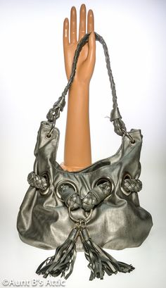 "80's to the Max!, vintage Bay Studio silver faux leather bucket style bag. Large silver metal rings hold the 18\" long braided handle. Another braided strap is woven through large silver metal rings in the front, and accented with 2 large tassels. The bag is lined with a leopard print cloth lining, and has 1 zippered pocket, and one open pocket. Snap strap closure. Bag sits on an oval base thats 7 1/2\" x 4 1/2\". Total height including strap-12\" Bag is in very good condition, and clean. *All Silver Leather Shoulder Bag As Fashion Accessory, Silver Leather Shoulder Bag With Hardware, Silver Hobo Bag With Silver-tone Hardware Tote, Silver Bucket Bag With Silver-tone Hardware For Everyday Use, Silver Hobo Bag With Silver-tone Hardware, Silver Shoulder Bag With Hardware For Everyday Use, Silver Bucket Bag With Silver-tone Hardware, Silver Tote Shoulder Bag With Metal Hardware, Large Tassels