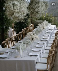 a long table is set with white flowers and place settings for an outdoor wedding reception