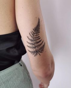 a woman's arm with a fern leaf tattoo on the back of her left arm