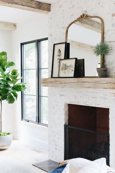 a living room with a fireplace, mirror and potted plant