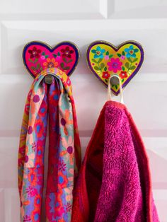 two colorful towels hanging from hooks on a white door with hearts and flowers painted on them