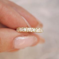 a woman's hand holding a gold ring with three stones on it and the band is