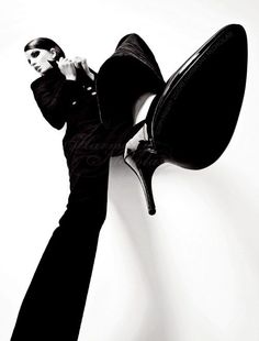 a woman leaning against a wall with her foot on the back of a black chair