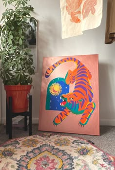 a painting is on the floor next to a potted plant and a rug with an orange tiger