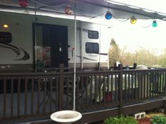 an rv parked on the side of a road next to a deck with lights hanging from it