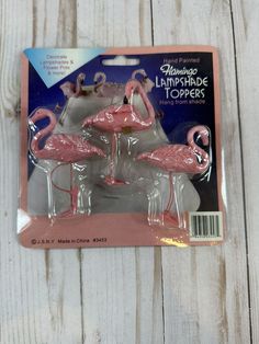 three pink flamingos sitting on top of each other in front of a white wooden background