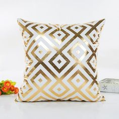 a gold and white pillow sitting on top of a table next to a vase with flowers