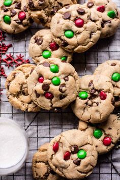 chocolate chip cookies with green and red candies on a cooling rack next to a glass of milk