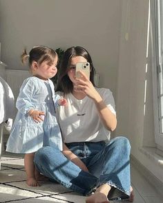 a woman taking a selfie with her daughter sitting on the floor next to a bed