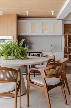 a table with chairs and plants on it in a room that has wooden cabinets, white tile flooring and walls