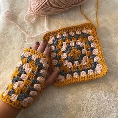 a woman's hand holding onto a crocheted square with yarn next to it