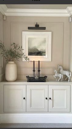 a white cabinet with two candles and a painting on it's wall above it