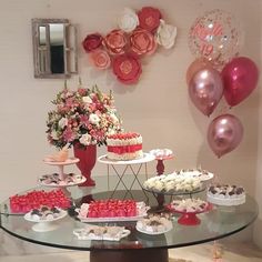 a table topped with lots of cakes and cupcakes next to pink balloons on the wall