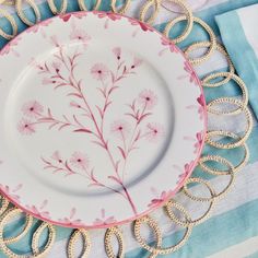 a white plate with pink flowers on it sitting on a blue and white table cloth