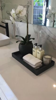 a bathroom counter with soap, toothbrushes and a flower in a vase on it