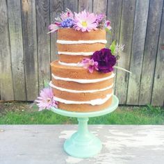 a three tiered cake with flowers on top is sitting on a table in front of a fence