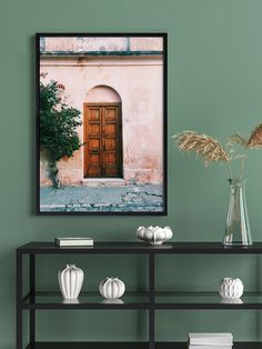 a green wall with a wooden door and vases on the shelf next to it