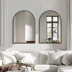 a living room with white furniture and two mirrors on the wall above it's windows