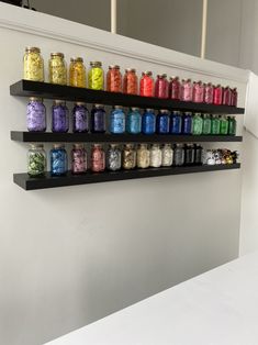 a shelf filled with lots of colorful jars on top of a white counter next to a mirror