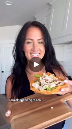 a woman is holding a pizza in her hands and smiling at the camera while she holds it up