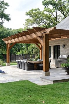 Wooden pergola over outdoor dining area with wicker chairs and table, next to a built-in grill on a stone patio in a garden. Porch With Pergola Attached, Large Pergola Patio Ideas, Pergola Patio Ideas Attached To House, Concrete Patio Pergola, Extended Patio With Pergola, How To Build A Patio Cover, Porch Covers On A Budget, Pergola Plans Attached To House, Covered Patio Ideas Attached To House