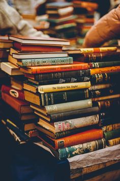 a stack of books sitting on top of a table next to a person's hand