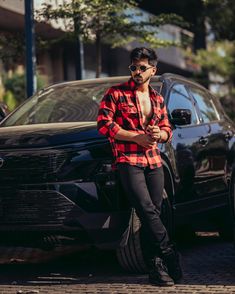 a man standing in front of a black car wearing sunglasses and a red flannel shirt