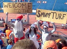 two people dressed as santa claus holding up signs in front of a crowd at a football game