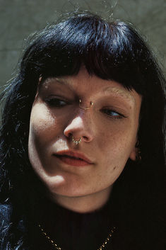 a woman with black hair and piercings on her nose is looking at the camera